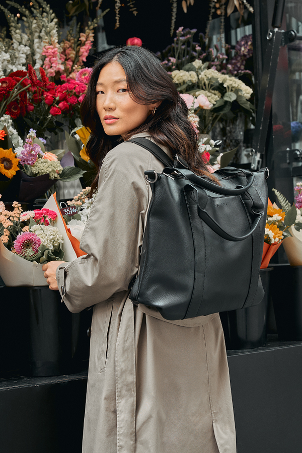 Woman with a black backpack standing in front of a flower stand.