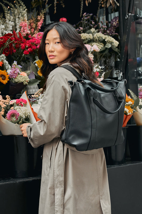 Woman with a black backpack standing in front of a flower stand.